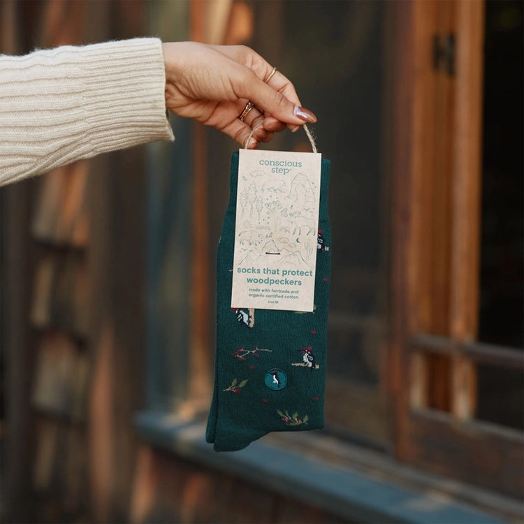Conscious Step woodpecker socks in forest green with gift packaging, held by hand