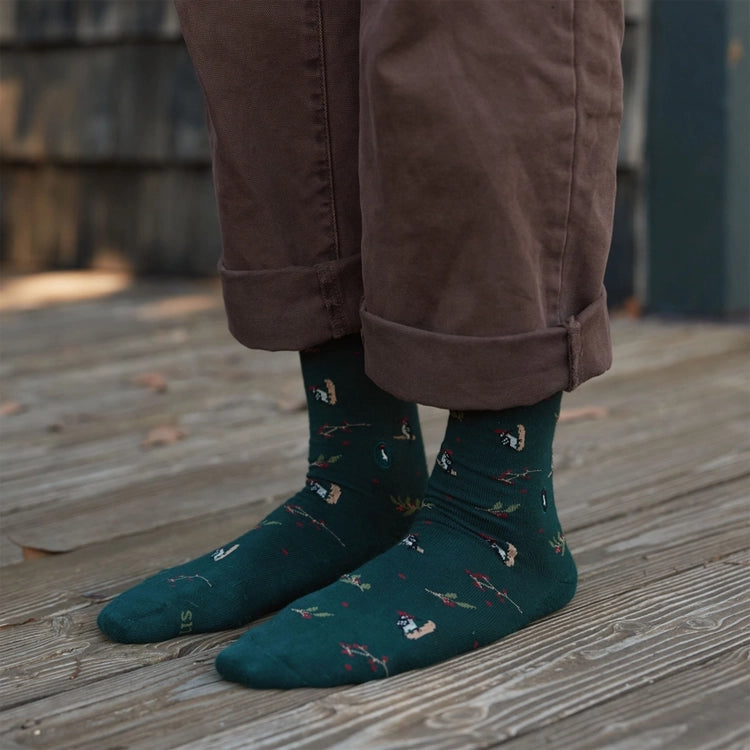 Person wearing forest green woodpecker socks with colorful bird and berry designs
