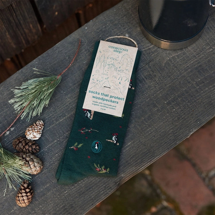 Conscious Step woodpecker socks with eco-friendly packaging displayed alongside pine branches and pinecones