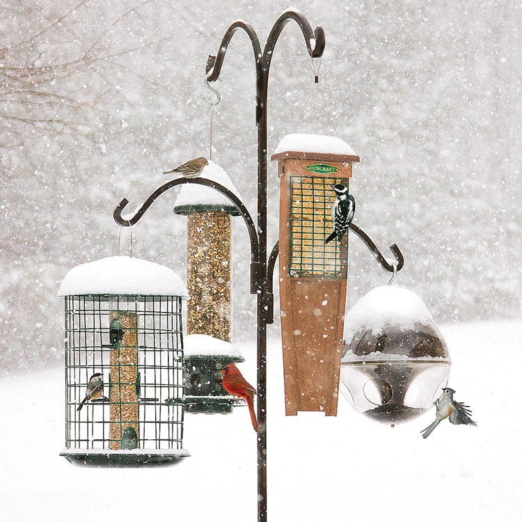 Bird feeders on a snowy day with birds perched on them.