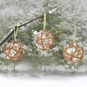 Grapevine Globes, Set of 3, hang from a snow-covered branch, each filled with suet, featuring a chickadee perched on the middle globe.
