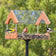 Duncraft Classic Platform Pole Feeder with birds eating, featuring brown sides, clear roof, and mounted on a 72-inch pole for easy placement and cleaning.