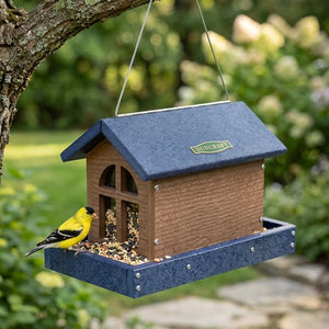 Barn bird feeder with seed and a bird hanging in the backyard showing the side view. 