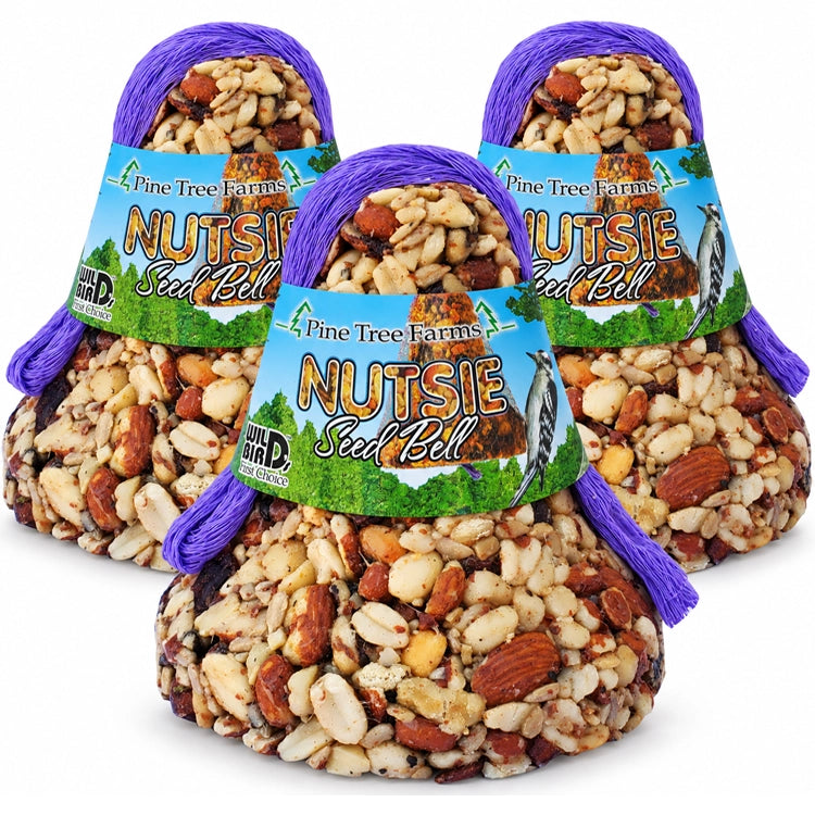 Three Pine Tree Farms Nutsie Seed Bells with blue and green labels and purple hanging loops on a white background.