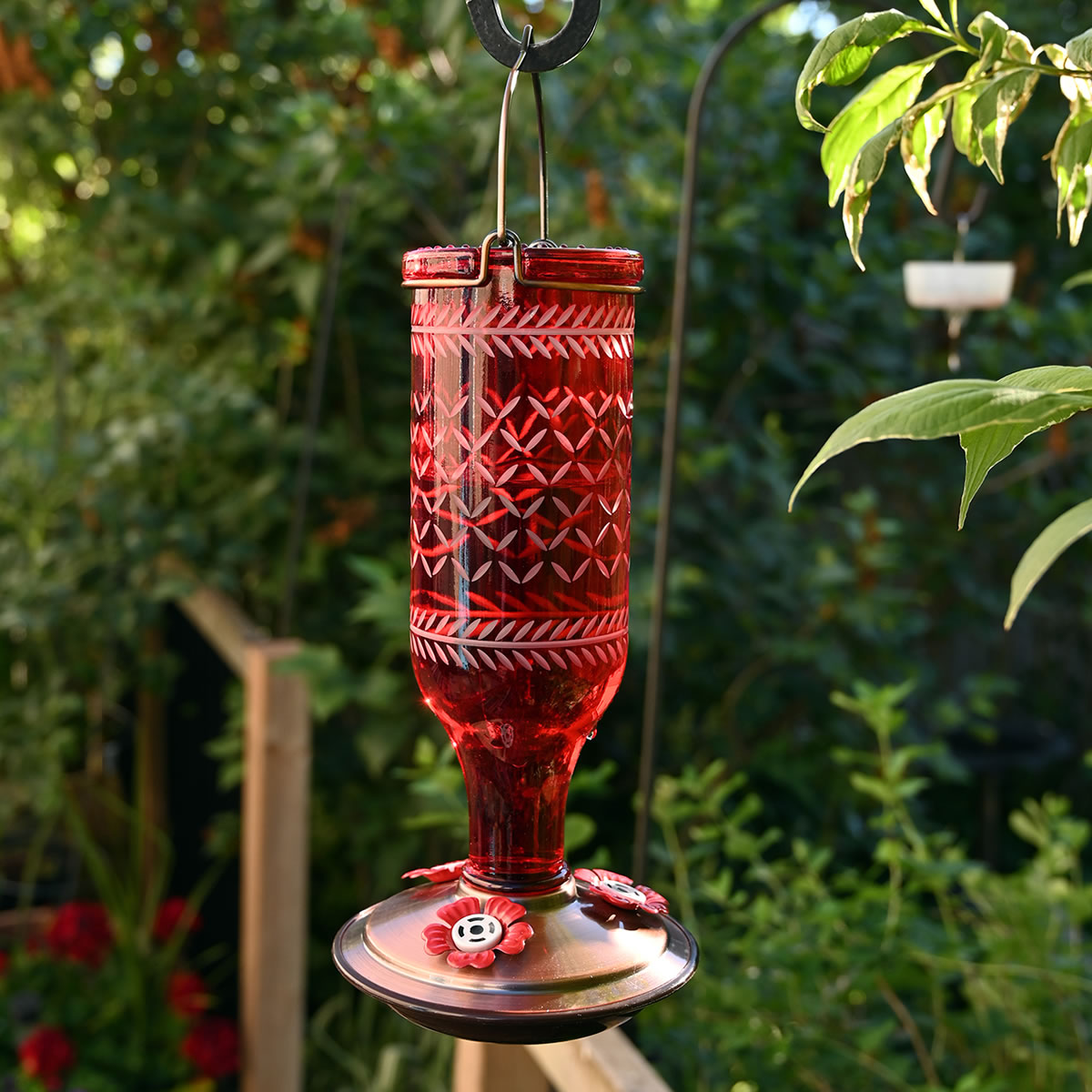 Vintage Bottle Style Glass Hummingbird Feeder with red flower-shaped ports, suspended from a hook, featuring a vintage-patterned glass bottle and metal base for garden decor.