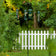 Bird feeders on a pole with a white picket fence and greenery in the background