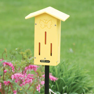 BirdsChoice Pole-Mounted Butterfly House, a yellow insect shelter on a black stake, among pink flowers in a garden, features decorative butterfly design.