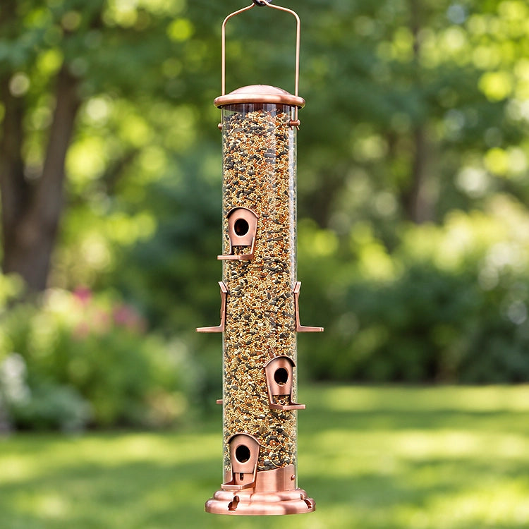 Copper tube bird feeder filled with mixed bird seed, featuring multiple feeding ports and perches, hanging in a lush green backyard.