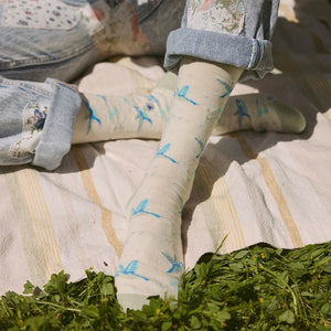 Close-up of cream hummingbird socks featuring blue birds in flight, worn with jeans during an outdoor picnic