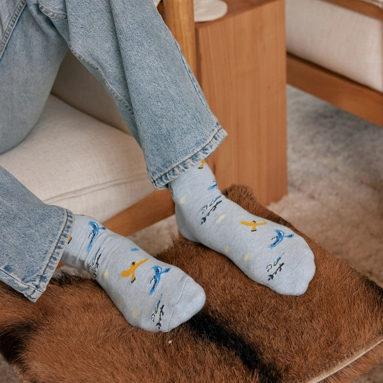 Person wearing light blue songbird socks with colorful bird designs and casual jeans