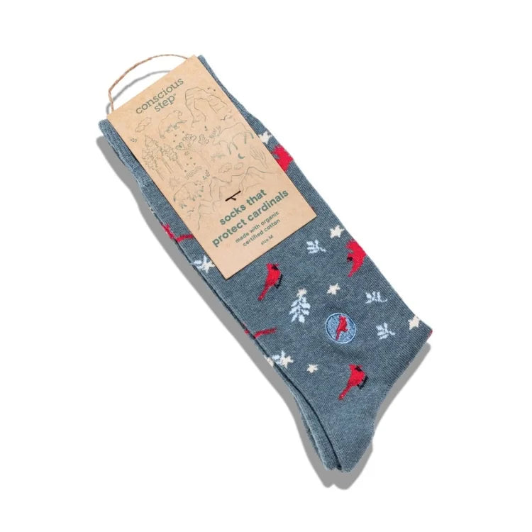 A pair of heathered slate blue socks with red cardinal and white snowflake patterns, packaged with a kraft paper tag that reads 'Corkcage Co. socks that protect cardinals'.