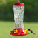 16 oz. Spiral Glass Hummingbird Feeder with a red lid, 6 feeding ports, and an S-hook for hanging, shown attracting a hummingbird.