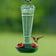 8 oz. Torchiere Glass Hummingbird Feeder with red flower ports and embossed green glass, attracting a hummingbird as it hovers to drink nectar.