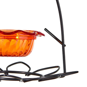 Close-up of an orange bird feeder with a black metal stand on a white background