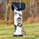 Two American Goldfinches perched on a birch log tube bird feeder with black roof in a backyard setting.