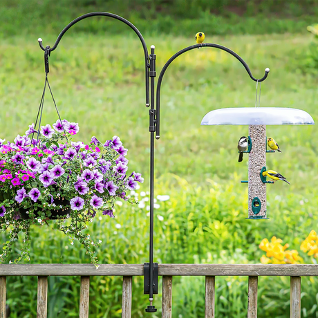 Platinum Cap Two Arm Clamp-On Deck Hanger with purple petunias and bird feeder, attracting yellow finches and a chickadee, mounted on a wooden deck railing.