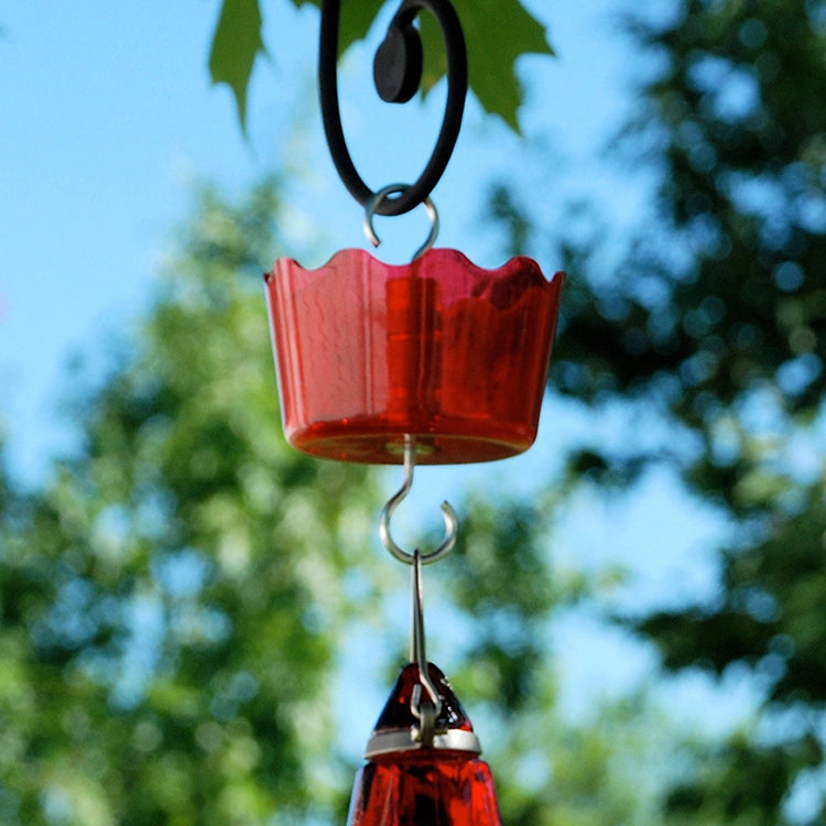 Red hummingbird feeder hanging against a blurred green and blue outdoor background