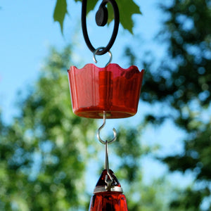 Red hummingbird feeder hanging against a blurred green and blue outdoor background