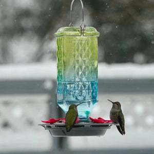 Antique-style ombre glass hummingbird feeder with textured glass reservoir, green-to-blue gradient finish, and red flower feeding ports.